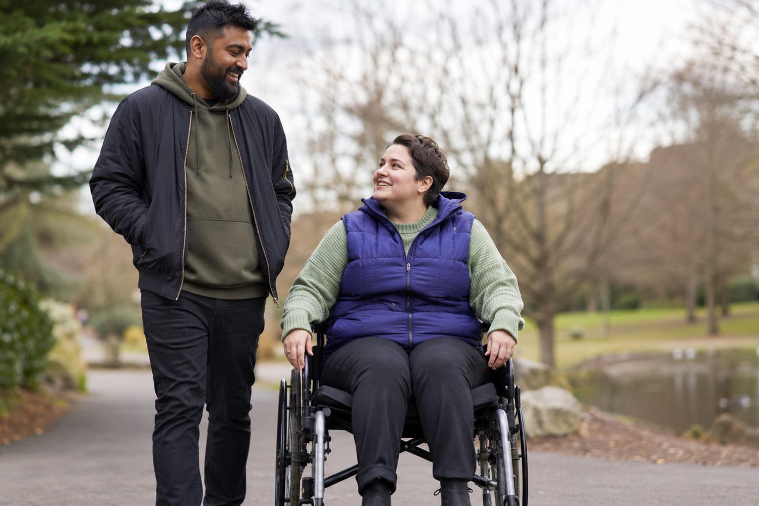 A support worker and a woman in a wheelchair enjoying a walk together through a leafy park